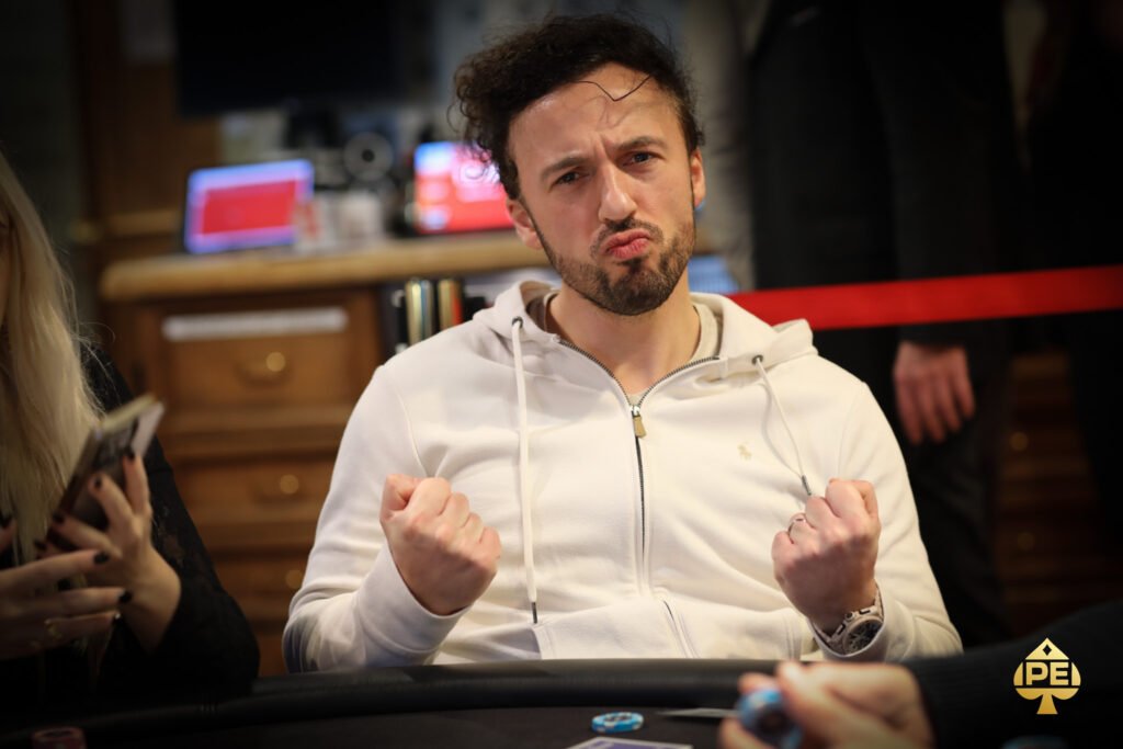 Ein Mann und eine Frau sitzen lächelnd an einem Pokertisch und halten Karten in der Hand. Die Frau hat eine Hand auf die Schulter des Mannes gelegt. Im Hintergrund sind Pokerchips und Getr