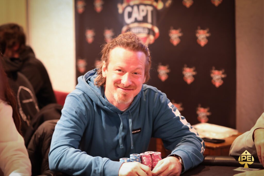 Ein Mann und eine Frau sitzen an einem Pokertisch und spielen Texas Hold'em. Der Mann hat einen Stapel Chips vor sich, während die Frau ihre Karten betrachtet. Die Szene spielt sich in einem eleganten Pokerra