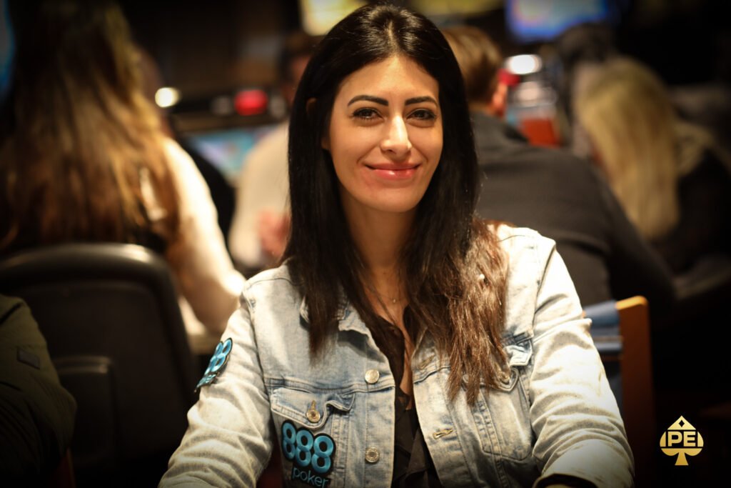 Ein professioneller Pokerspieler in einem dunkelblauen Anzug und einer dunklen Sonnenbrille sitzt an einem Pokertisch mit grünem Filz. Er hält seine Karten in der Hand und wirkt kon