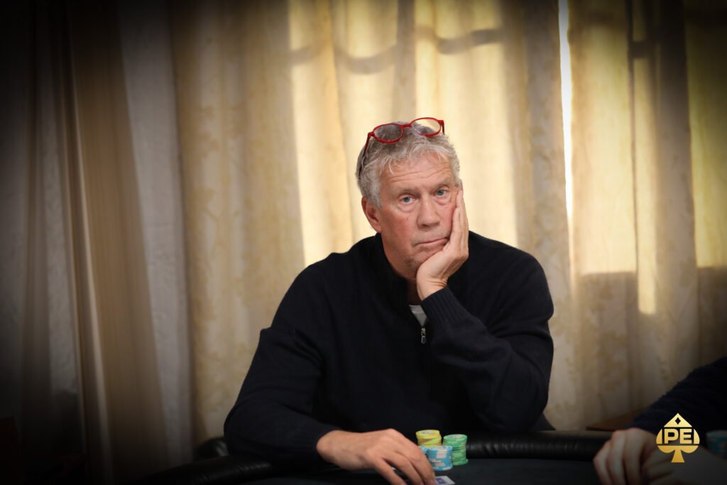 Ein professionelles Pokerturnier mit mehreren Spielern an einem Tisch, die ihre Karten betrachten und ihre Einsätze machen. In der Mitte des Tisches liegen Pokerchips und Spielkarten. Die Spieler tragen eleg
