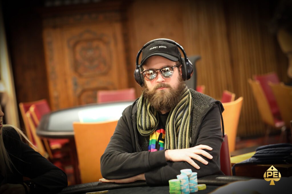 Ein professioneller Pokerspieler mit Sonnenbrille und Kopfhörern konzentriert sich am Tisch auf seine Karten während eines Turniers.