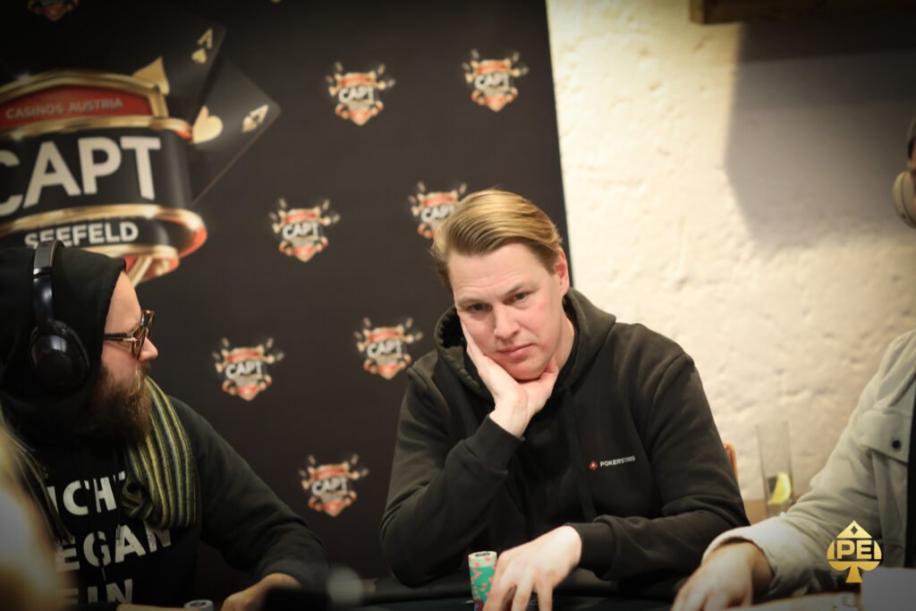 Ein Paar Männer spielen Poker an einem eleganten Tisch in einem luxuriösen Casino. Die Männer sind konzentriert und haben Stapel von Chips vor sich liegen. Die Szene strahlt eine Atmosphäre von Span