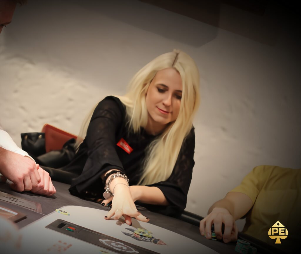 Ein Mann in einem schwarzen Anzug und einer Krawatte sitzt an einem Pokertisch und hält seine Karten in der Hand, während er konzentriert auf die Mitte des Tisches schaut. Um ihn herum