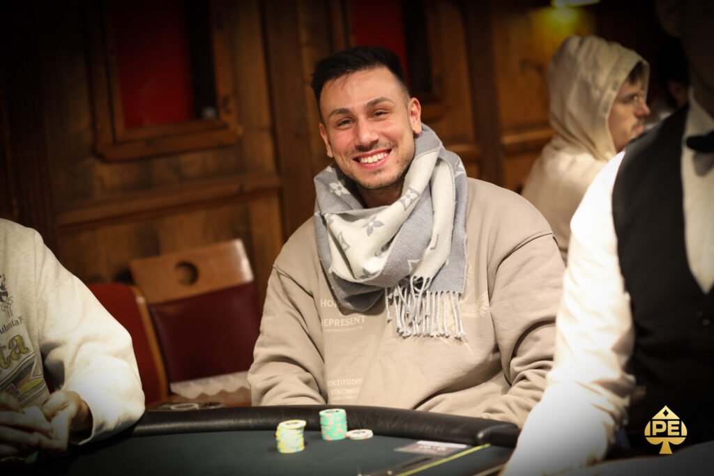 Ein Mann in einem schwarzen Anzug und einer schwarzen Sonnenbrille spielt Poker an einem eleganten Tisch in einem luxuriösen Casino. Er hält Karten in der Hand und hat einen ernsten Gesichtsaus
