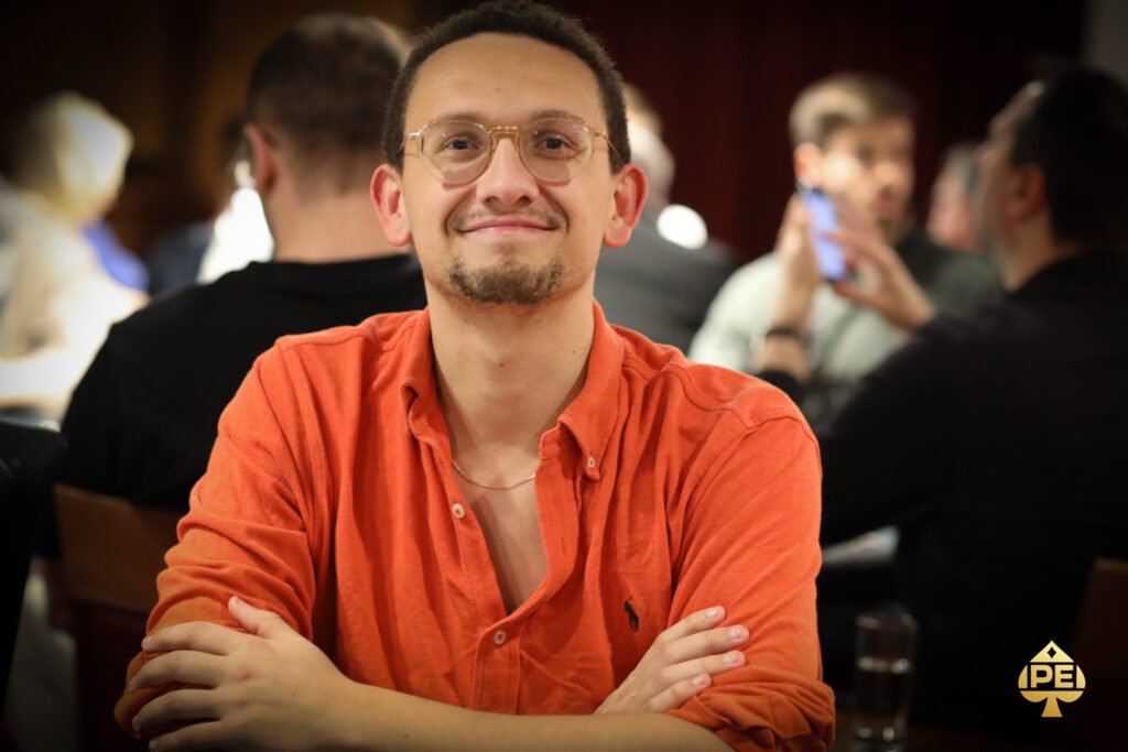 Ein Mann mit schwarzer Sonnenbrille sitzt an einem Pokertisch und hält seine Karten in der Hand, während er konzentriert auf seine Gegner schaut.