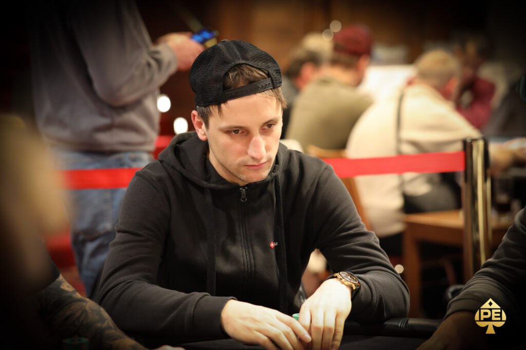 Ein professioneller Pokerspieler mit Sonnenbrille und Kopfhörern sitzt an einem Pokertisch mit Chips und Karten.