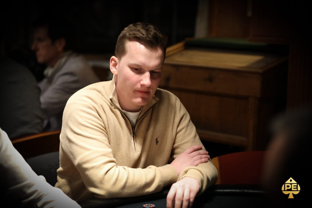 Ein Mann und eine Frau sitzen an einem Pokertisch und spielen eine Partie Poker. Der Mann hat eine Hand mit Karten vor sich liegen, während die Frau ihre Karten noch hält. Im Hintergrund sind Pokerchips