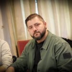Ein Mann und eine Frau sitzen an einem Pokertisch in einem eleganten Casino. Der Mann hat gerade seine Karten aufgedeckt und die Frau schaut gespannt auf ihre eigenen Karten. Die Atmosphäre ist konzent