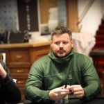 Ein Mann und eine Frau spielen Poker am Tisch in einem eleganten Casino. Der Mann hat eine Hand mit Spielkarten, während die Frau konzentriert ihre Karten betrachtet. Ein Stapel Jetons liegt vor ihnen auf dem