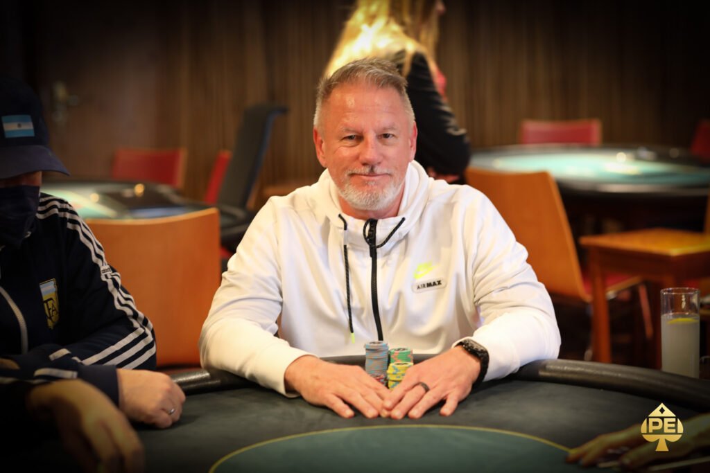 Ein Mann und eine Frau sitzen am Pokertisch und halten ihre Karten. Sie haben konzentrierte Gesichtsausdrücke. Um sie herum sind Pokerchips und Getränke zu sehen.