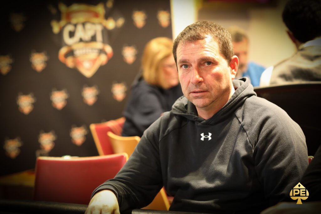 Ein Mann und eine Frau sitzen an einem Pokertisch und betrachten konzentriert ihre Karten. Im Hintergrund sind Pokerchips und Spielkarten auf dem Tisch zu sehen.