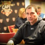 Ein Mann und eine Frau sitzen an einem Pokertisch und betrachten konzentriert ihre Karten. Im Hintergrund sind Pokerchips und Spielkarten auf dem Tisch zu sehen.
