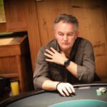 Ein bunter Pokertisch mit Spielkarten, Chips und Getränken, umgeben von verschiedenen Personen, die konzentriert und gespannt spielen.