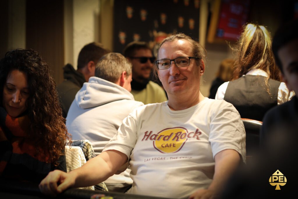 Ein professioneller Pokertisch mit grüner Filzoberfläche, umgeben von Spielkarten, Pokerchips und Getränken. Mehrere Spieler sitzen um den Tisch herum und konzentrieren sich auf
