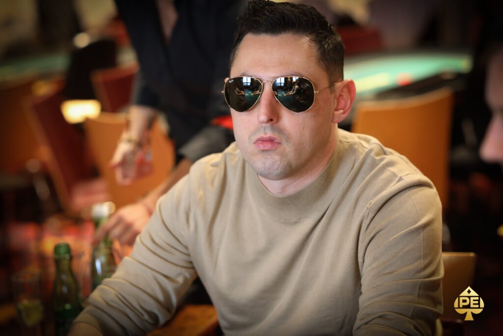 Ein Mann und eine Frau sitzen an einem Pokertisch und betrachten konzentriert ihre Karten. Der Mann hat einen Stapel Chips vor sich liegen, während die Frau mit einem ernsten Gesichtsausdruck ihre Hand