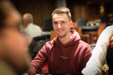 Ein Mann mit dunklen Haaren und einem Anzug sitzt an einem Pokertisch und betrachtet konzentriert seine Karten.