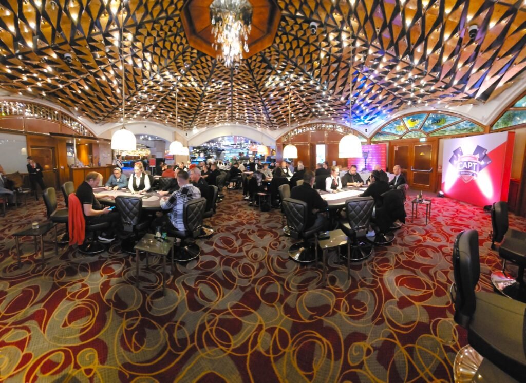 Ein bunter Pokertisch mit Spielkarten, Pokerchips und Getränken, umgeben von Personen, die Poker spielen und Spaß haben.
