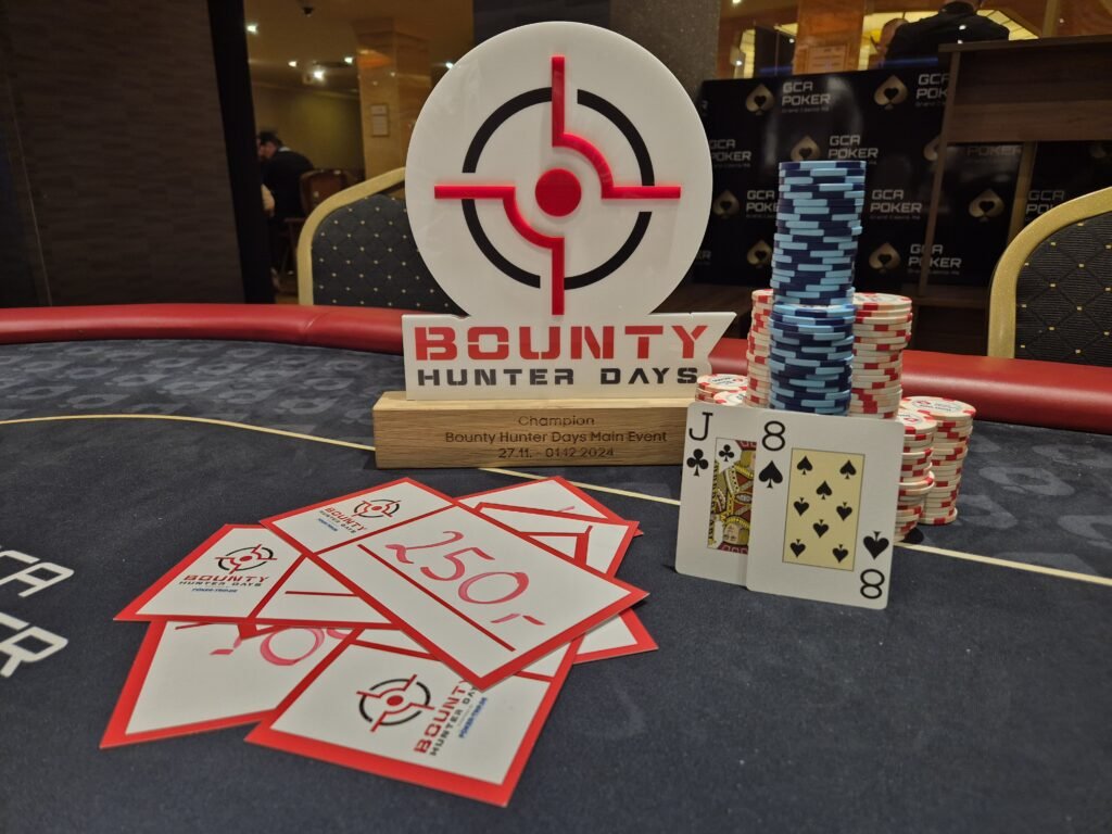 Ein Mann sitzt an einem Pokertisch und hält zwei Karten in der Hand, während er konzentriert auf seine Gegner schaut.
