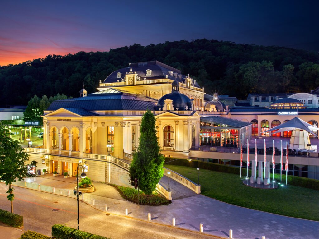 Ein eleganter und moderner Innenraum eines Casinos mit stilvoller Beleuchtung, hochwertigen Möbeln und einer ansprechenden Dekoration. Es gibt Spieltische, Stühle und eine Bar im Hinter