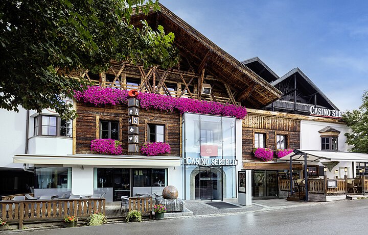 Ein eleganter Pokertisch mit grünem Filz, umgeben von Stühlen und Spielern, die Karten halten und Chips stapeln, in einem stilvollen Casino in Seefeld.