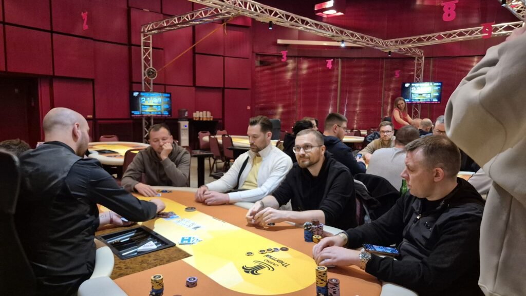 Ein professioneller Pokertisch mit grünem Filz, umgeben von Spielkarten, Pokerchips und Getränken, während Spieler in einem spannenden Spiel involviert sind.
