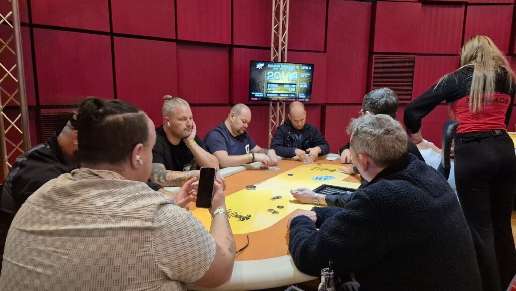 Ein Mann spielt Poker an einem Tisch in einem Casino, umgeben von anderen Spielern. Er hält Karten in der Hand und betrachtet konzentriert die Chips vor ihm.