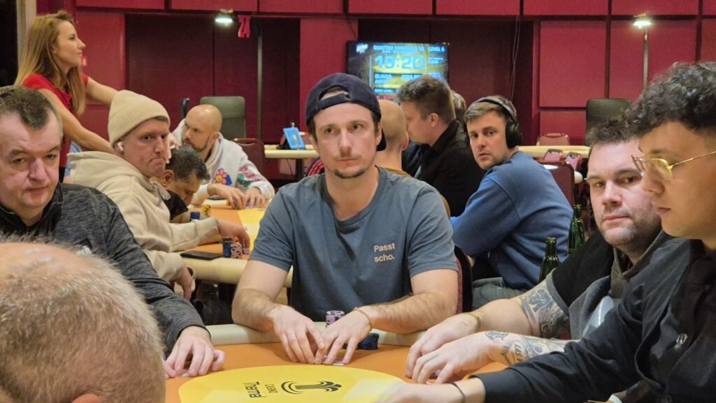 Ein Mann und eine Frau sitzen an einem Pokertisch und spielen mit Pokerchips und Karten. Der Mann hat eine Hand am Kinn und schaut nachdenklich, während die Frau konzentriert ihre Karten betracht