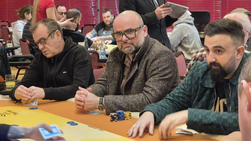 Ein professioneller Pokertisch mit grüner Filzoberfläche, umgeben von Stühlen und Chips. In der Mitte des Tisches befinden sich Spielkarten und Spieler, die ihre Hände überprüfen.