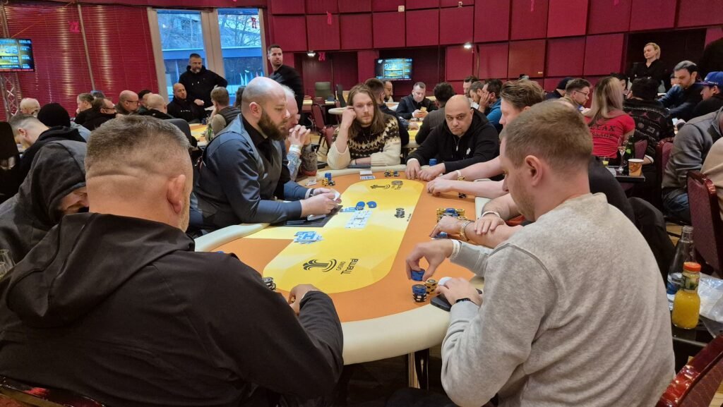 Ein Mann spielt Poker an einem Tisch in einem Casino, umgeben von anderen Spielern und Chips.