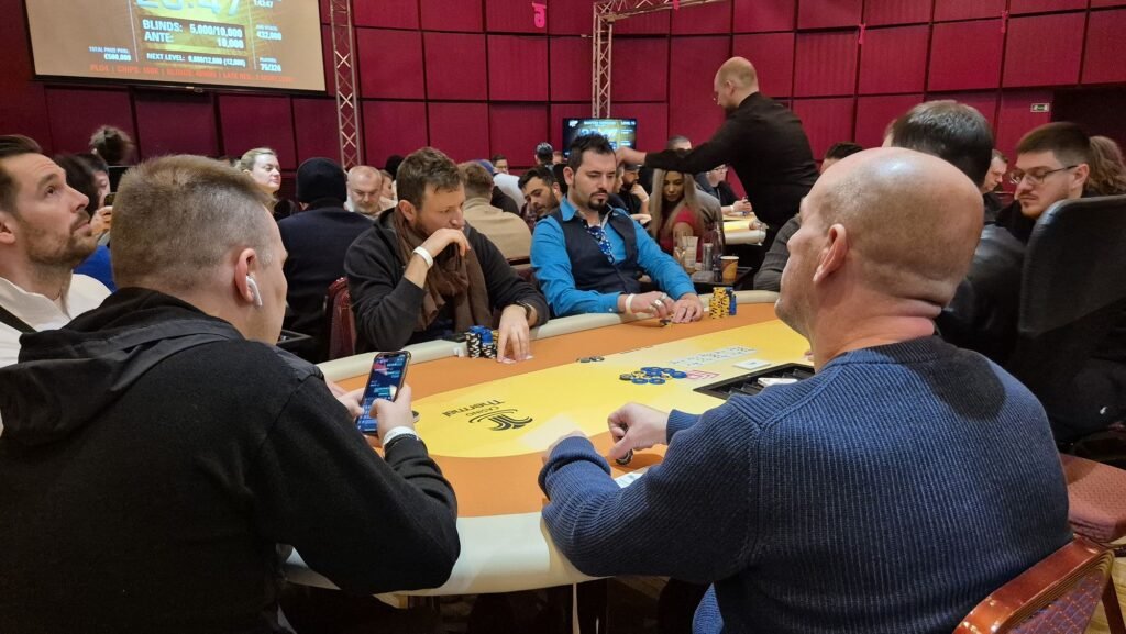 Ein Mann in einem schwarzen Anzug sitzt an einem Pokertisch und hält zwei Könige (König-König) in der Hand. Er schaut konzentriert auf seine Karten, während Chips vor ihm