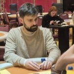 Ein professioneller Pokertisch mit grünem Filz und einem Kartendeck in der Mitte, umgeben von Pokerchips und Getränken. Im Hintergrund sind Spieler und Dealer zu sehen, die Karten halten und