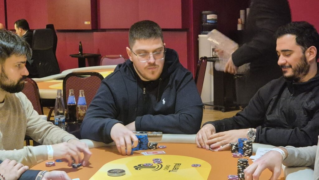 Ein professioneller Pokertisch mit grünem Filz, umgeben von Spielern, die Karten halten und Chips stapeln.