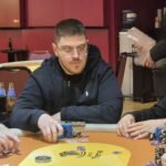 Ein professioneller Pokertisch mit grünem Filz, umgeben von Spielern, die Karten halten und Chips stapeln.
