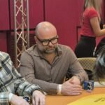 Ein professioneller Pokertisch mit grünem Filz, umgeben von Stühlen und Spielchips, während Spieler ihre Karten halten und setzen.