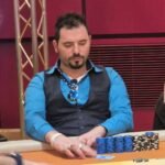 Ein professioneller Pokertisch mit grünem Filz und neun Sitzplätzen, umgeben von Spielkarten, Pokerchips und Getränken. Zwei Spieler sind in einer intensiven Hand, während andere ges