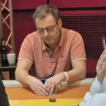 Ein professioneller Pokerspieler mit Sonnenbrille und einem Stapel Pokerchips vor sich sitzt an einem Pokertisch und betrachtet konzentriert seine Karten.