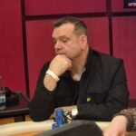 Ein professioneller Pokerspieler mit Sonnenbrille und einem Stapel Pokerchips vor sich, der konzentriert seine Karten betrachtet.