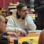 Ein Mann spielt Poker in einem eleganten Kasino, umgeben von anderen Spielern und einer glamourösen Atmosphäre.