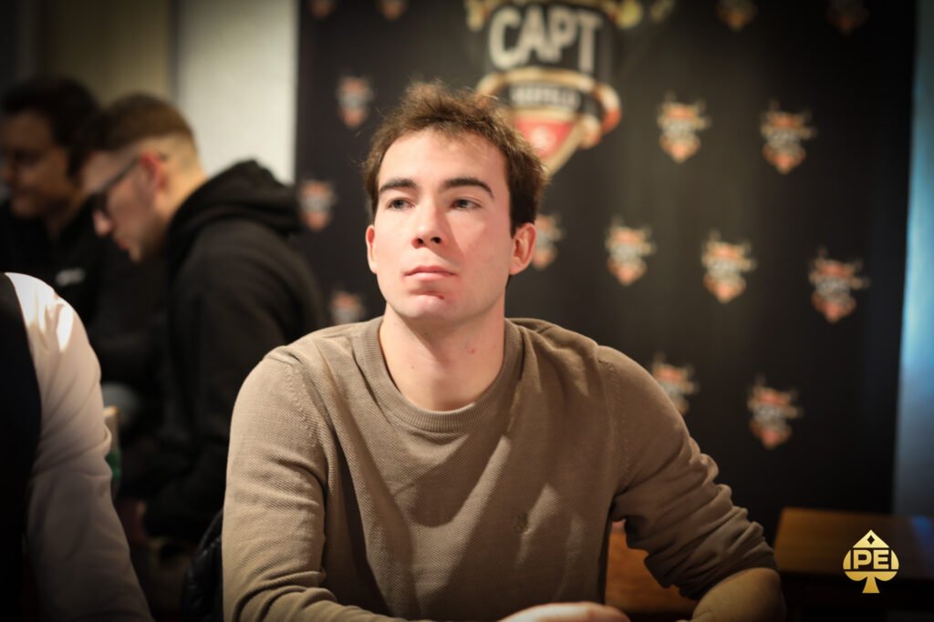Ein Mann und eine Frau sitzen an einem Pokertisch und spielen Texas Hold'em. Der Mann hat einen Pokerchip in der Hand und schaut konzentriert auf seine Karten, während die Frau mit ernstem Gesichtsausdr