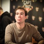 Ein Mann und eine Frau sitzen an einem Pokertisch und spielen Texas Hold'em. Der Mann hat einen Pokerchip in der Hand und schaut konzentriert auf seine Karten, während die Frau mit ernstem Gesichtsausdr