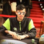 Ein Mann und eine Frau sitzen an einem Pokertisch und betrachten konzentriert ihre Karten. Im Hintergrund sind Pokerchips und Getränke zu sehen.