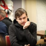 Ein Mann und eine Frau sitzen an einem Pokertisch und spielen Texas Hold'em. Der Mann hält Karten in der Hand und schaut konzentriert auf den Tisch, während die Frau mit gespielter Gelassenheit ihre