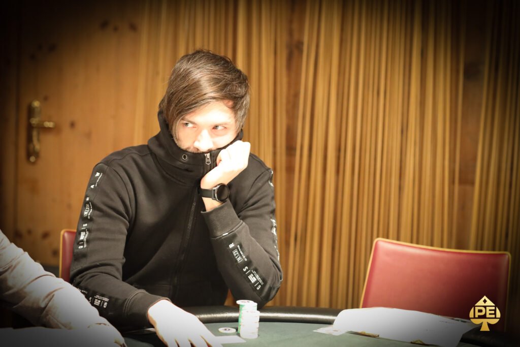 Ein Mann und eine Frau sitzen lächelnd an einem Pokertisch, während sie Karten halten und Chips stapeln. Die Frau hat blonde Haare und trägt ein rotes Oberteil, der Mann hat dunkle Haare
