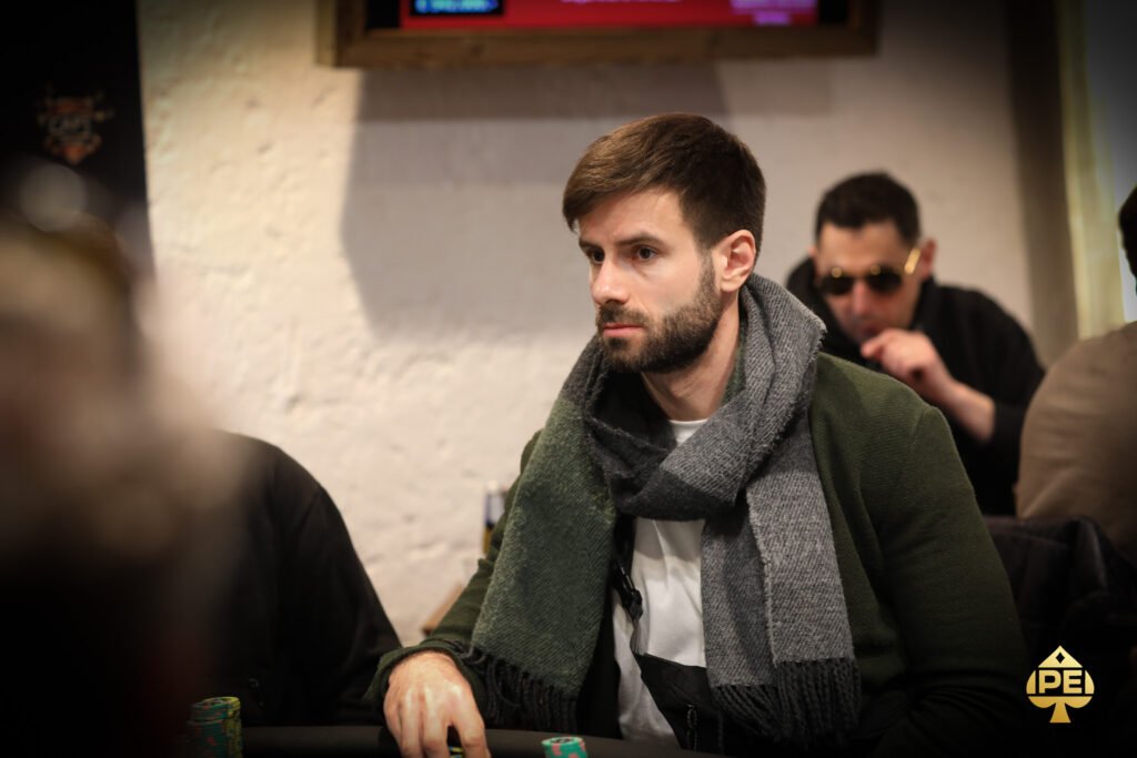 Ein Mann und eine Frau sitzen an einem Pokertisch und spielen Poker. Der Mann hat gerade Karten ausgeteilt und schaut konzentriert auf seine Hand, während die Frau lächelnd ihre Karten betrachtet