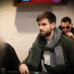Ein Mann und eine Frau sitzen an einem Pokertisch und spielen Poker. Der Mann hat gerade Karten ausgeteilt und schaut konzentriert auf seine Hand, während die Frau lächelnd ihre Karten betrachtet