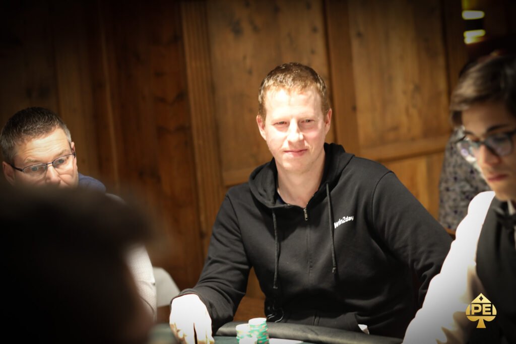 Ein Mann und eine Frau sitzen an einem Pokertisch und betrachten konzentriert ihre Karten. Ein Stapel Chips und ein Dealer Button sind auf dem Tisch zu sehen. Die Atmosphäre ist ernst und spannungsg
