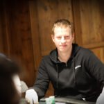 Ein Mann und eine Frau sitzen an einem Pokertisch und betrachten konzentriert ihre Karten. Ein Stapel Chips und ein Dealer Button sind auf dem Tisch zu sehen. Die Atmosphäre ist ernst und spannungsg