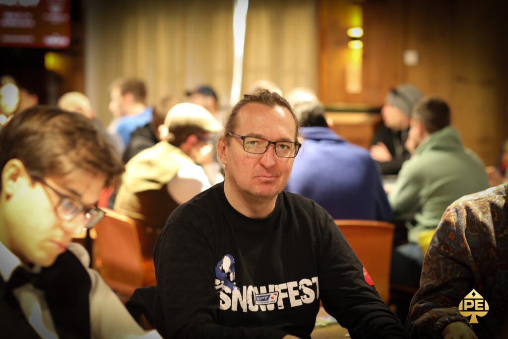 Ein professioneller Pokertisch mit grünem Filz, umgeben von Stühlen und Spielkarten, Chips und Getränken. Zwei Personen sitzen am Tisch und halten ihre Karten, während sie konzentri