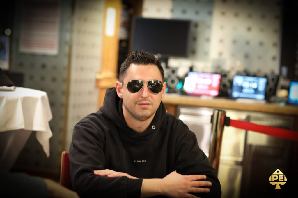 Ein Mann und eine Frau sitzen an einem Pokertisch und betrachten konzentriert ihre Karten. Eine grüne Pokertischdecke ist zu sehen, sowie Pokerchips und Spielkarten. Die Frau trägt eine