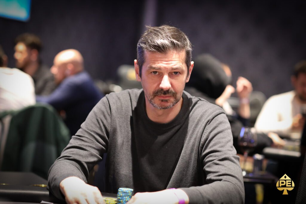 Ein Mann und eine Frau spielen Poker an einem eleganten Tisch in einem stilvollen Casino. Die Frau hält Karten in der Hand, während der Mann konzentriert auf seine Karten schaut. Um sie herum befinden